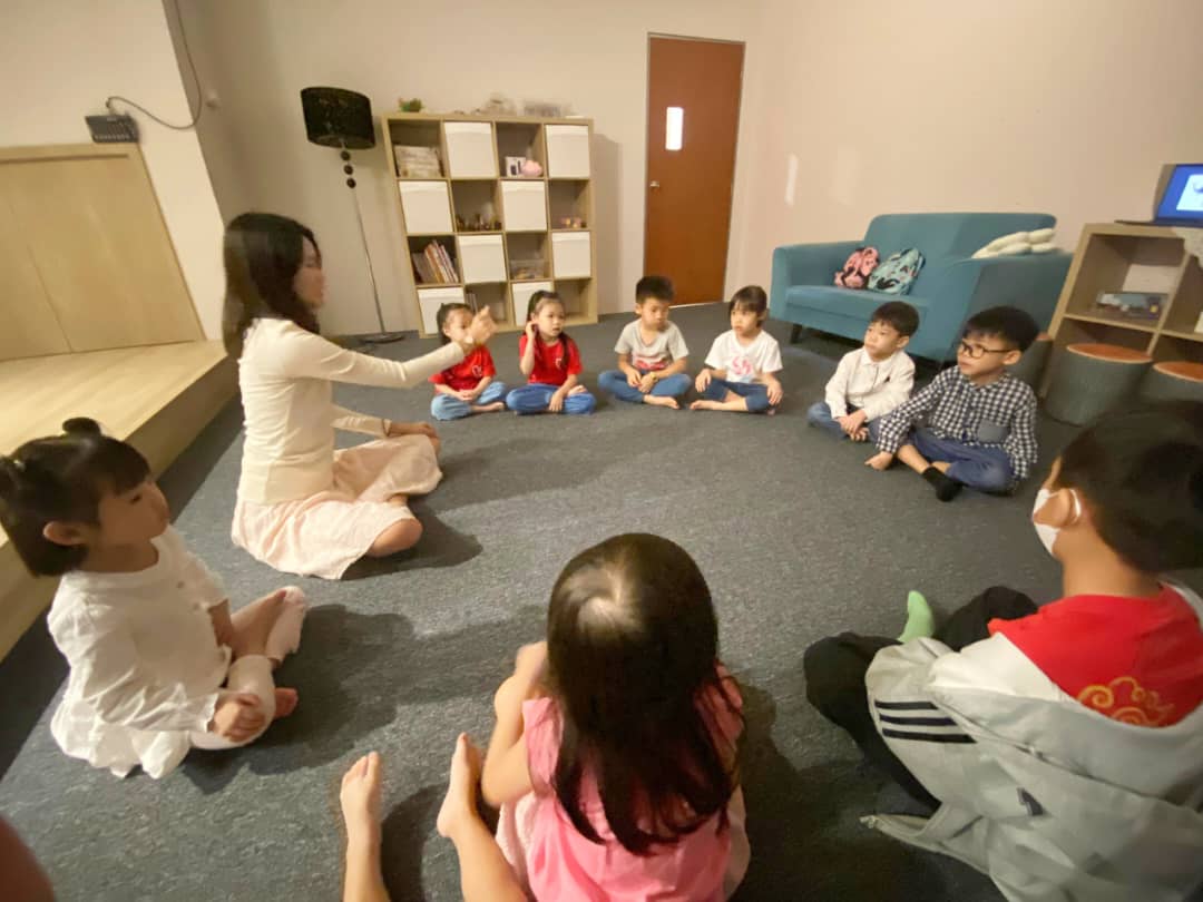 孩子们盘腿坐成一圈，看着老师并举手回应